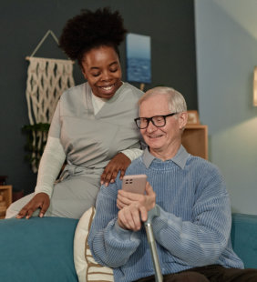female caregiver and elderly man smiling while looking at smartphone