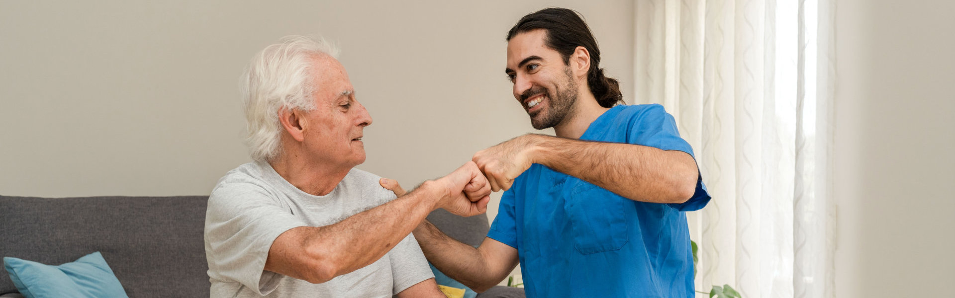 male caregiver doing fist bump with elderly man